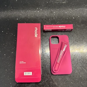 Rhode Lip Case för iPhone - Snyggt och praktiskt Rhode Lip Case i rosa, designat för iPhone. Fodralet har en integrerad hållare för medföljande lip tint. Produkten ser oanvänd ut och levereras med originalförpackning. Perfekt för dig som vill kombinera stil och funktion.