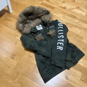 Päls hoddie från hollister  - Snygg trendig hoodie från Hollister i mörkgrön camouflage med stor fluffig fuskpäls på huvan. Hoodien har dragkedja, broderad logga på bröstet och stor vit text längs ärmen.  Detta är huvudligen ett intress koll eftersom jag älskar detta plagg men behöver pengar, har du frågor skriv gärna! 💕❤️