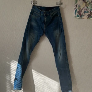 Blå jeans från G-Star RAW - Säljer ett par snygga blå jeans från G-Star RAW med klassisk femficksdesign och läderpatch bak. Jeansen har en något tvättad look och raka ben. Perfekta för dig som gillar stilrena och bekväma jeans med coola detaljer. Storlek W30 L 34