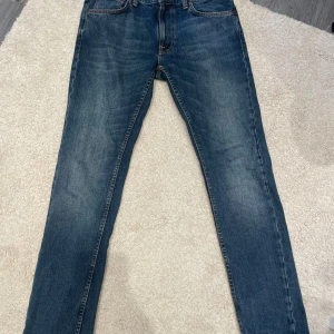 Nudie Jeans Lean Dean blå jeans 31/32 - Säljer ett par Nudie Jeans Lean Dean i tvätten Troubled Sea. Klassiska blå jeans med smal passform, orangea sömmar och fem fickor. Materialet är 99% bomull och 1% elastan för lite stretch. Perfekta för dig som gillar en modern och stilren look.
