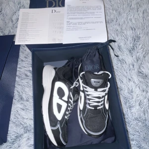 Dior B30 svarta sneakers med reflex - Säljer ett par Dior B30 sneakers i svart med vita och reflekterande detaljer. Skorna har tydlig Dior-logga på sidan, vit sula och svarta meshpaneler. Klassisk snörning och sportig design. Kommer med originalkartong, dustbag och extra skosnören.