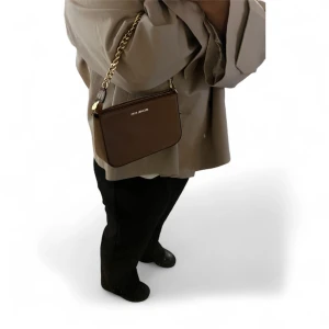 Michael Kors Brun axelväska  - Snygg brun axelväska från Michael Kors i skinn med guldfärgad kedja och dragkedja upptill. Väskan har en stilren, rektangulär form och diskret logga framtill. Perfekt storlek för det viktigaste och enkel att matcha med olika outfits.