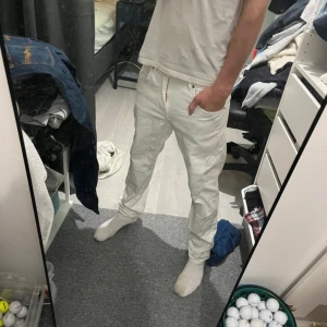 Vita jeans från J.Lindeberg 31/32 - Säljer ett par fräscha vita jeans från J.Lindeberg i storlek 31/32. Byxorna har klassisk femficksdesign, bälteshällor och diskret JL-logga på fickan. Snygg passform med raka ben och tillverkade i bomull för en skön känsla.