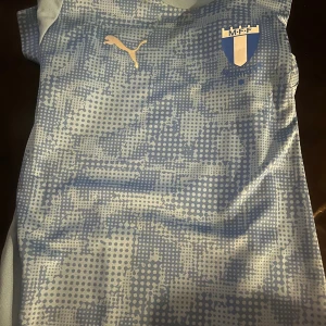 Malmö FF kortärmad fotbollströja Puma - Snygg ljusblå fotbollströja från Puma med Malmö FF-logga på bröstet. Tröjan har ett prickigt mönster framtill och är tillverkad i ett lätt, ventilerande material som passar perfekt för träning eller match. Klassisk kortärmad modell med rund hals.