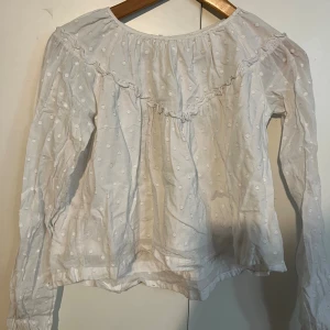 Vit prickig blus från Gina Tricot - Supersöt vit blus från Gina Tricot med diskreta prickar i tyget och volangdetalj över bröstet. Långärmad modell med rynkade ärmslut och knapp i nacken. Perfekt för en fräsch och luftig look.