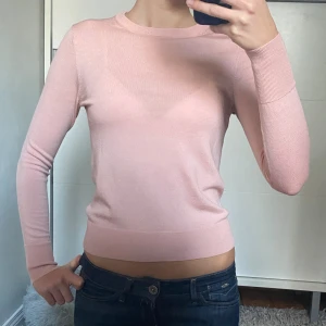 Ljusrosa stickad tröja - Säljer en ljusrosa stickad tröja i 100% ull med rund halsringning och långa ärmar. Tröjan har en slim passform och är tillverkad i ett mjukt, tunt material som sitter supersnyggt. Perfekt att styla med jeans nu till hösten. 
