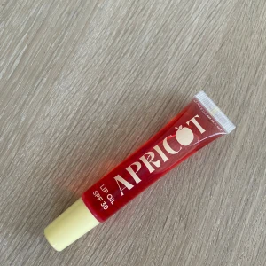 Apricot Lip Oil SPF 30 - Superfräsch läppolja i klarröd tub med SPF 30 från Makeup Mekka. Ger glansiga, återfuktade läppar och har en söt aprikosdoft. Perfekt att ha i väskan för en juicy look och skydd mot solen.