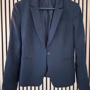 Tiger of Sweden kavaj - Elegant svart kavaj från Tiger of Sweden.  Officina by Marlane. Klassisk design och enkel knappstängning. Perfekt för en stilren look. Kavajen har en smickrande passform och är tillverkad i ett bekvämt material. Strukturmönstrad med dold knapp vid ärmslut. 