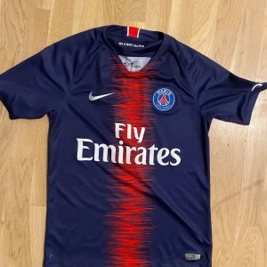 PSG Mbappé matchtröja Nike S - Paris Saint-Germain fotbollströja med Mbappé och nummer 7 på ryggen. Mörkblå med röd och vit grafisk effekt i mitten, PSG-emblem på bröstet och Fly Emirates-tryck. Tillverkad i lätt Dri-Fit polyester för bästa komfort på planen.