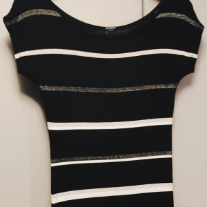 Randig långklänning från Calzedonia - Svart långklänning med vita och glittriga silverfärgade horisontella ränder. Klänningen har rund hals och korta ärmar, figurnära passform och är gjord i mjukt syntetmaterial. Perfekt för dig som gillar stilrena och trendiga mönster. Nyskick. 