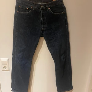 Levi's 501 mörkblå jeans W32 L32 - Klassiska Levi's 501 jeans i mörkblå denim med raka ben och femficksmodell. Byxorna har knäppning fram, tydliga kontrastsömmar och den ikoniska läderpatchen bak i midjan. Perfekta för dig som gillar tidlös stil och schysst passform.