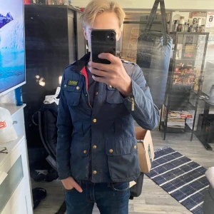 Blå Barbour jacka med svarta detaljer - Snygg blå jacka från Barbour. Ger en rikigt fräsch och Grisch look perfekt för dig som vill se clean ut. Passar perfekt för xs