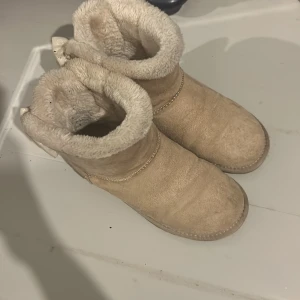 Beiga uggs med rosett från Ashton Aubry - Mysiga beiga boots från Ashton Aubry i mocka med fluffigt foder och stora rosetter bak, dekorerade med pärlor. Storlek 37. Använda cirka 15ggr. Säljer pga köpt nya.😊❣️