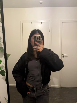 Svart bomberjacka från Gina Tricot - Jackan har en snygg croppad passform och silverfärgad dragkedja framtill.