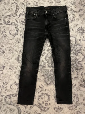 Nudie jeans Lean Dean - Svarta jeans från Nudie Jeans med ganska skinny passform och klassisk femficksdesign. Jeansen har svarta sömmar, subtila slitningar och Nudie Jeans logga på bakfickan. Materialet är stretchigt denim för en bekväm känsla. Modellen är Lean Dean och storleken 29 32. För fler frågor eller funderingar är det bara att höra av sig MVH