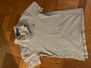 Grå pikétröja från Polo Ralph Lauren - Snygg och fräsch grå pikétröja från Polo Ralph Lauren i slim fit-modell. Klassisk krage, korta ärmar och två knappar framtill. Broderad logga på bröstet. Perfekt för att visa upp lite biceps för tösarna✌️Passar även XS, org pris 1500, skick 9/10