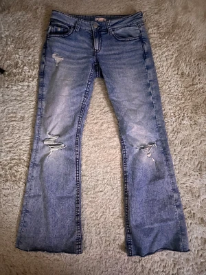 Flare ljusblå jeans med slitningar - Flare jeans i ljusblå tvätt med slitna detaljer på båda benen. Klassisk femficksmodell med knapp och dragkedja framtill samt bakfickor med lock och knapp. Jeansen har en avslappnad flare-passform och är tillverkade i denim.