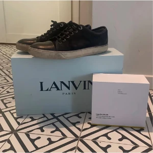 Svarta sneakers från Lanvin  - Svarta sneakers från Lanvin.  Klassisk och stilren design med metallöglor och beige innersula. Perfekta för dig som gillar exklusiva och tidlösa sneakers. OBS inte original skosnören passar 42