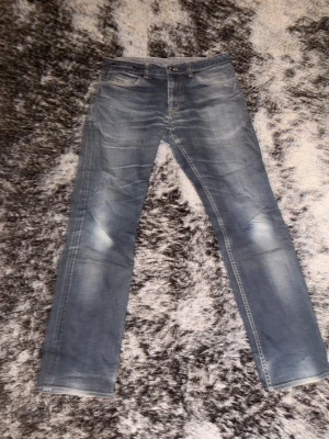 Blå raka jeans med slitningar - Snygga blå jeans med klassisk femficksdesign och ljusa slitningar på låren. Jeansen har raka ben och kontrastsömmar i gult, vilket ger en cool vintagekänsla. Passar dig som gillar en tidlös look och vill ha jeans som funkar till det mesta.