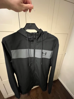Svart vindjacka från Under Armour XS - Svart vindjacka från Under Armour i storlek XS perfekt för dig som gillar sportig stil och vill ha något lätt och funktionellt. Inga defekter 