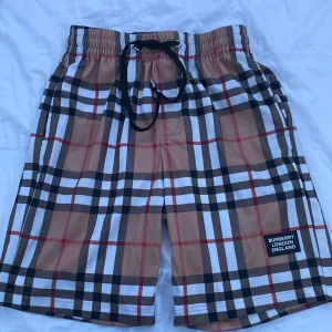 Rutig shorts från Burberry - Säljer ett par snygga shorts från Burberry i klassiskt rutigt mönster. De är i beige, svart, vit och röd. Storlek M men passar S perfekt. Funkar som vanliga shorts och badbyxor 