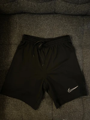 Svarta träningsshorts - Svarta shorts från Nike med elastisk midja med snörning. Passar 11-12Y.