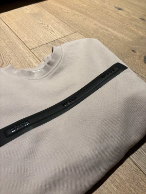 Beige sweatshirt från BOSS - PASSAR DIG OM DU ÄR MELLAN 169cm - 176 cm Snygg beige sweatshirt från BOSS med svart, upphöjd logga på bröstet. Tröjan har rund hals, långa ärmar och ribbade muddar vid ärmslut och nederkant. Materialet är mjukt och känns som bomull, perfekt för en chill och stilren look.