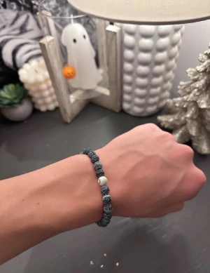Svart och vit pärlarmband med mönster - Unikt armband med svarta och vita pärlor, där de svarta pärlorna har ett coolt nätliknande mönster. En vit pärla med öga-detalj ger extra karaktär. Perfekt accessoar för dig som gillar att sticka ut med detaljer och mönster.
