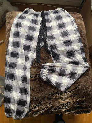 Rutiga pyjamasbyxor med spets - Rutiga byxor i svart och vitt med elastisk midja och muddar vid bensluten. Snygg detalj med svart spets framtill som ger en unik look. Perfekta för dig som gillar att sticka ut med din stil.