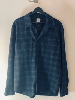 Mörkblå rutig overshirt från Zara - Snygg mörkblå skjorta från Zara med rutigt mönster och klassisk krage. Modellen heter The Melange Shirt och har två bröstfickor med knappar. Skjortan är långärmad och har en loose passform, perfekt för en chill och stilren look.