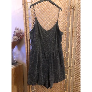 Glittrig svart jumpsuit från H&M Divided - Supersnygg svart glittrig kortklänning från H&M Divided med tunna axelband och v-ringning. Jumpsuiten har en lätt utställd kjol och skimrande material som fångar ljuset. Perfekt för dig som vill sticka ut med en trendig look. Skön att ha på sig också!