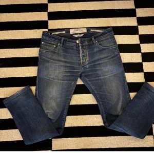 Blå jeans från Jacob Cohën Style 622 - Snygga blå jeans från Jacob Cohën, modell Style 622. Klassisk femficksdesign med guldfärgade knappar och brunt läderpatch bak. Jeansen har en rak passform och är tillverkade i mjukt denimtyg med subtila slitningar för en cool look.