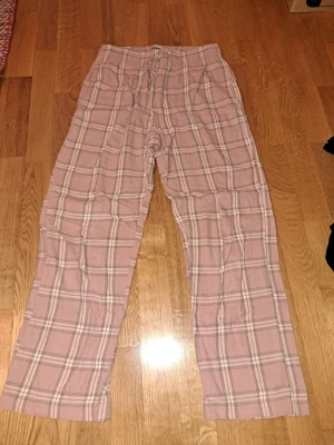Rosa rutiga pyjamasbyxor byxor från 157 - Säljer ett par chill rosa pyjamasbyxor från 157 med grått och vitt rutmönster. Byxorna har elastisk midja med snörning och raka ben. Perfekta för att hänga hemma eller mysa i soffan. Mjukt bomullsmaterial som är skönt mot huden. Fickor på båda sidorna.