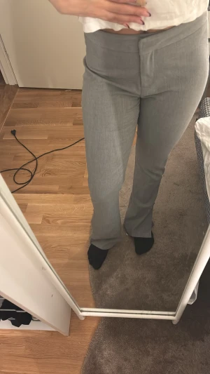 Grå kostymbyxor med bootcut - Snygga grå kostymbyxor med bootcut-snitt och hög midja. Byxorna har en stilren design med dold knäppning framtill och diskreta fickor bak. Materialet känns mjukt och har en lätt struktur som ger en dressad vibe.