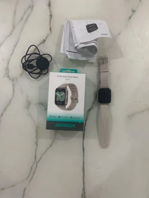 Beige smartklocka från Joyroom - Säljer en beige Joyroom Fit-life Series Smart Watch med fyrkantig display och silikonarmband. Klockan har en modern look och kommer med laddare och manual. Perfekt för dig som vill ha koll på träning och hälsa direkt på handleden.