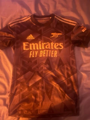 Arsenal Ødegaard bortatröja Adidas XS - Säljer en svart Arsenal bortatröja från Adidas i storlek XS med Ødegaard och nummer 8 på ryggen. Tröjan har geometriskt mönster, guldiga detaljer och klassiska Adidas-ränder på axlarna. Materialet är lätt och andas, perfekt för fotboll eller att bära till vardags. Från säsongen 22/23, jag köpte den ny 1200 kr 