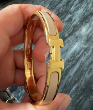 H armband harmens beige guld  -  armband i guld och beige med H-detalj.