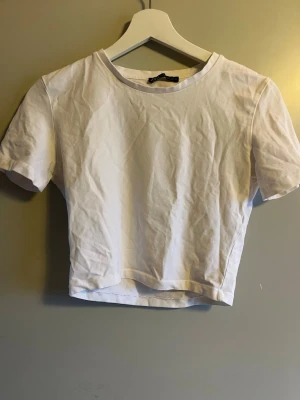 Vit croppad t-shirt från Zara - En enkel och fräsch vit croppad t-shirt från Zara. Modellen har rund hals och korta ärmar, perfekt för dig som gillar en clean och stilren look. Tillverkad i mjuk bomull som känns skön mot huden. Passar dig som vill ha en basic topp med modern passform.
