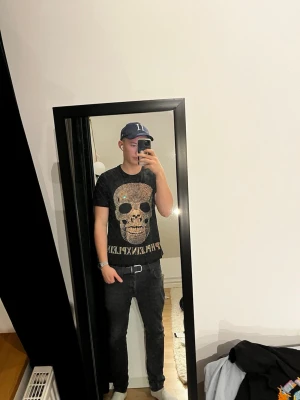 Philipp Plein t-shirt - Säljer en svart t-shirt från Philipp Plein med stor glittrig döskalle framtill och guldfärgad logga under. T-shirten har korta ärmar och en normal passform. Perfekt för dig som gillar edgy och lyxig streetstyle.