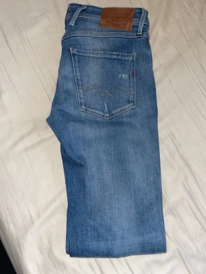 Replay ljusblå jeans med slitningar - Snygga ljusblå jeans från Replay med klassisk femficksdesign och slitna detaljer, inklusive en större reva på ena benet. Jeansen har rak passform och är tillverkade i mjukt denim-material med skinnpatch bak i midjan.