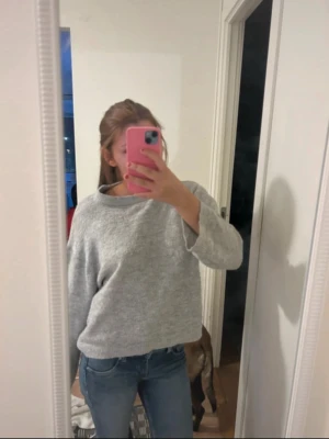 Grå stickad tröja med rund hals - Säljer en enkel och snygg grå stickad tröja med rund hals och lång ärm. Tröjan har en loose passform och är perfekt att slänga på sig när det är lite kyligt ute. Passar till jeans eller andra favoritbyxor.