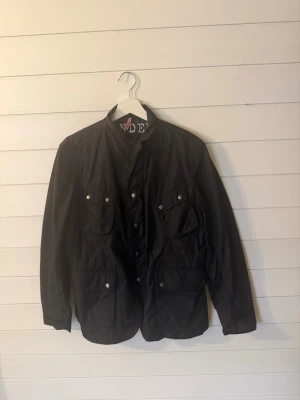 Svart vindjacka från J.Lindeberg - Svart vindjacka från J.Lindeberg med broderad text på insidan. Jackan har fyra framfickor med knappar, ståkrage och snygga detaljer. Materialet är lätt och känns sportigt, perfekt för dig som gillar stilren design. Skick 9/10 använd endast några gånger nypris ligger på cirka 4000kr. Priset kan diskuteras, hör av dig vid frågor🤩