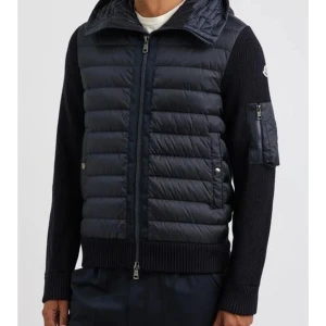 Mörkblå Moncler cardigan - Säljer en mörkblå pufferjacka från Moncler med stickade ärmar och huva. Jackan har dragkedja framtill, fickor med tryckknappar och en extra ficka med dragkedja på ärmen. Moncler-logga på vänster ärm. Perfekt för höst och vinter. Storlek 3 sitter som M-L