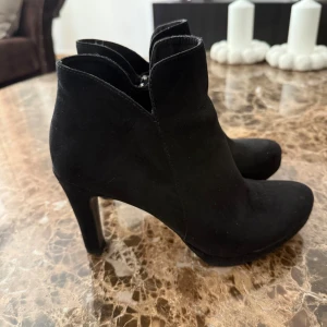 Svarta stövletter med klack - Snygga svarta stövletter i mocka med hög klack och spetsig tå. Perfekta för dig som vill ha en stilren och trendig look. Skorna har en elegant siluett och passar till många olika outfits.