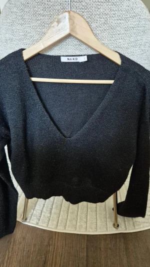 Svart stickad tröja NA-KD - Svart stickad tröja från NA-KD med djup v-ringning och lång ärm. Tröjan är mjuk och har en loose passform, perfekt för lager-på-lager. Materialet är 80% akryl och 20% polyamid, vilket gör den lätt och skön att bära. Kortare modell.