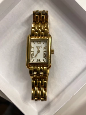 Guldfärgad rektangulär klocka Regal - Snygg guldfärgad klocka från Regal med rektangulärt ur och länkarmband i metall. Urtavlan är vit med romerska siffror i guld och har en klassisk, stilren look. Perfekt accessoar för dig som gillar tidlös design och vill sticka ut. Man får med två extra delar ifall man skulle vilja göra den längre!!!!!⚠️⚠️⚠️