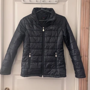 Svart quiltad pufferjacka Covalliero - Svart pufferjacka från Covalliero med quiltad design och hög krage. Jackan har två fickor med dragkedja och raka ärmar. Materialet är glansigt och lätt, perfekt för kyliga dagar. Stängs med dragkedja framtill och har en stilren look.