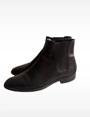 Saint Laurent Chelsea Boots Hedi Slimane - Klassiska svarta chelsea boots från Saint Laurent i slätt skinn. Snygg minimalistisk design med rund tå och elastiska paneler på sidorna för enkel påtagning. Perfekta för dig som gillar stilrena och tidlösa skor med lyxig känsla. Låda medföljer ej, men skickas i bra förpackning. Kan passa en 44:a :)