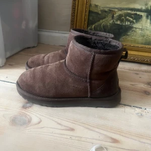 Bruna UGG boots i mocka - Mörkbruna UGGs i mkt bra skick. Klassisk UGG-logga baktill och kort skaft. Kan skicka med orginalkartongen om så önskas!🤗 kan mötas upp i Stockholm 26-30 nov