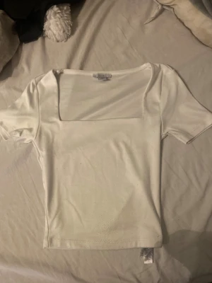 Vit topp  XS - Vit topp från new yorker i storlek XS med korta ärmar och snygg fyrkantig ringning. Toppens material känns mjukt och stretchigt, perfekt för en clean och stilren look. Enkel att matcha med olika outfits.